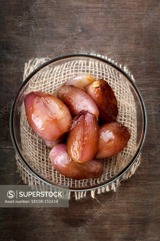 Pickled shallots in a glass bowl on wooden table, studio shot