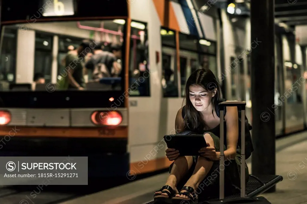 Portrait of young woman waiting at tram stop by night using tablet