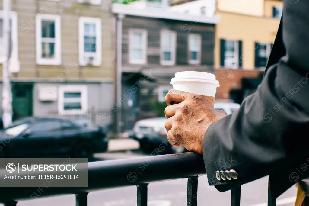 Hands of a man holding cup of coffee on railing
