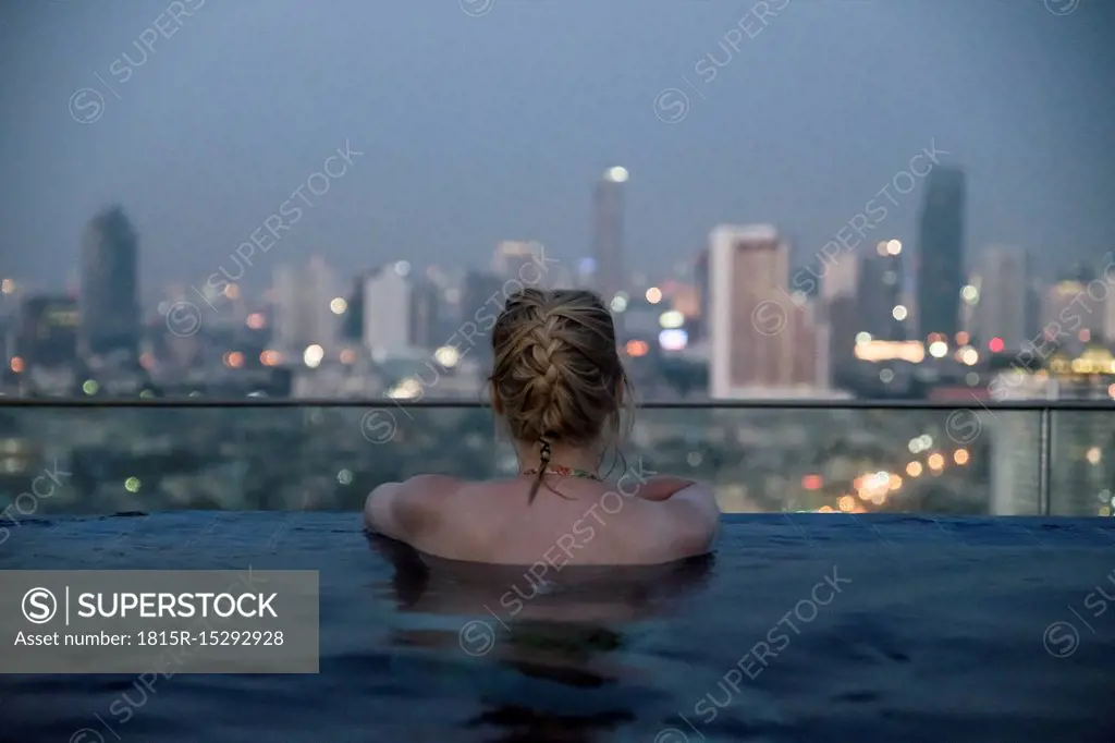 Thailand, Bangkok, back view of woman bathing in Infinity Pool looking at skyline