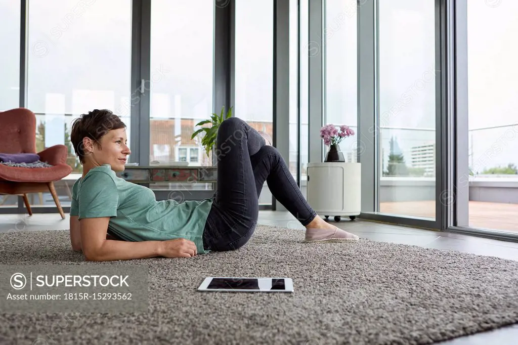Woman lying on the floor at home with tablet looking out of balcony door