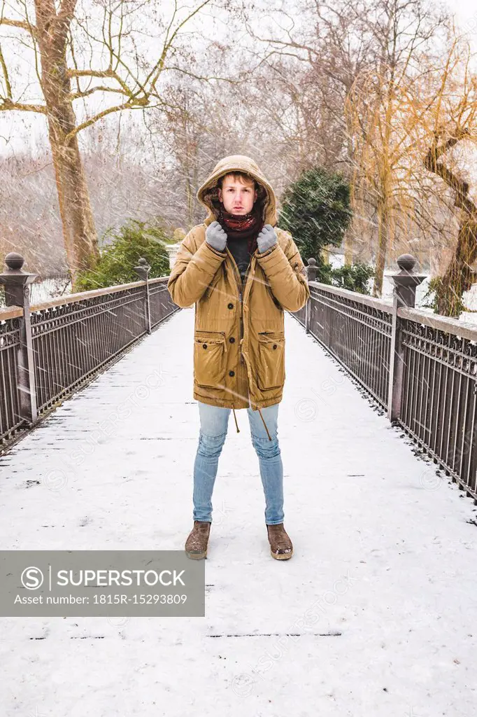 Young man standing on footbridge in a park on a snowy day