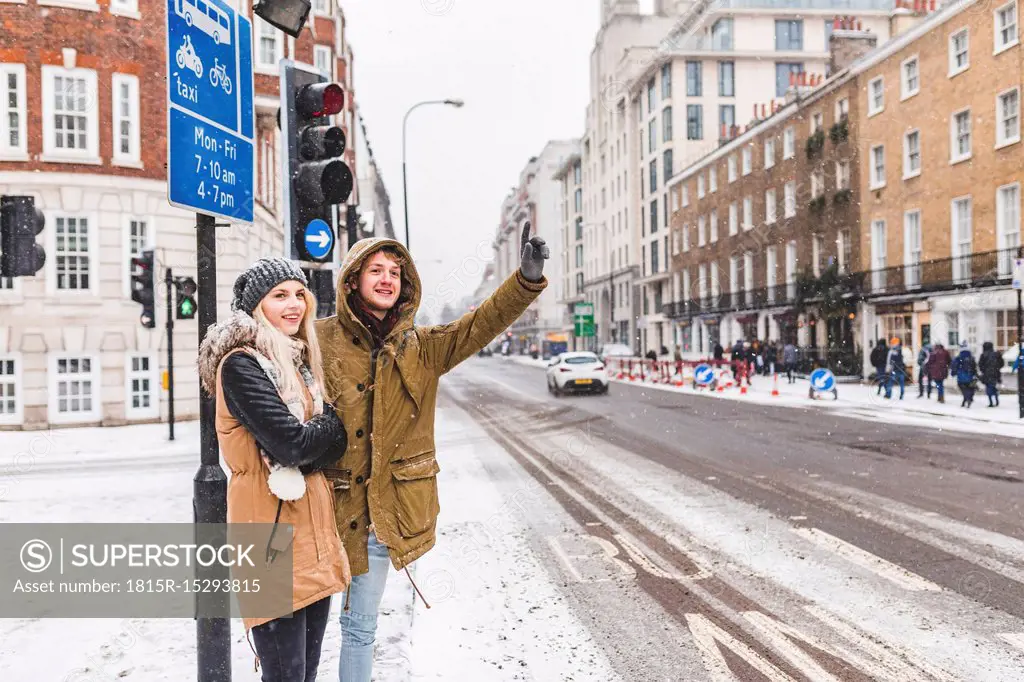UK, London, young couple standing at roadside hailing taxi in winter