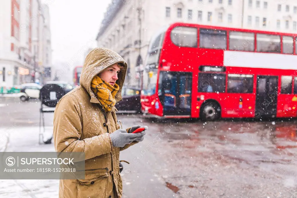 UK, London, young man with cell phone standing at roadside looking at distance