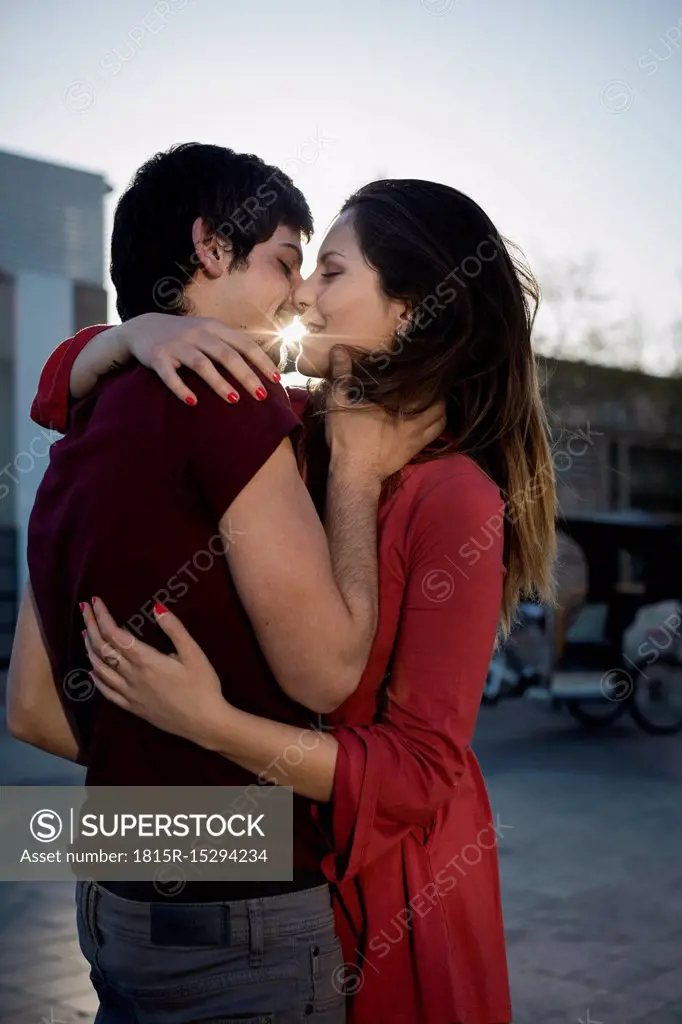 Affectionate young couple hugging and kissing on city square at sunset