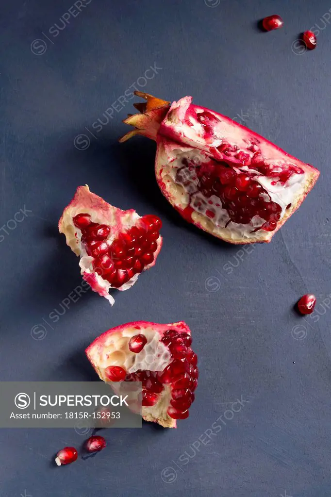 Pits and three pieces of pomegranate Punica granatum on blue wood, studio shot