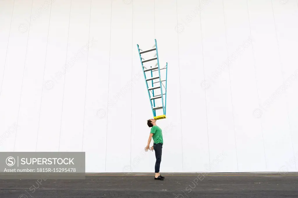 Acrobat balancing ladder on his face - SuperStock