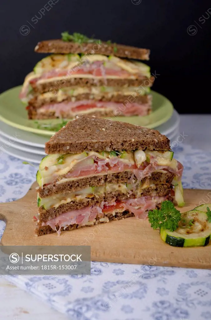 Whole-grain bread sandwiches with ham, roasted zucchinis, tomatoes and cheese on plate and on chopping board garnished with cress, studio shot