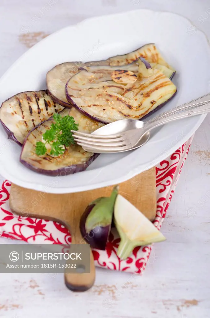Roasted slices of eggplant on plate standing on wooden chopping board, studio shot