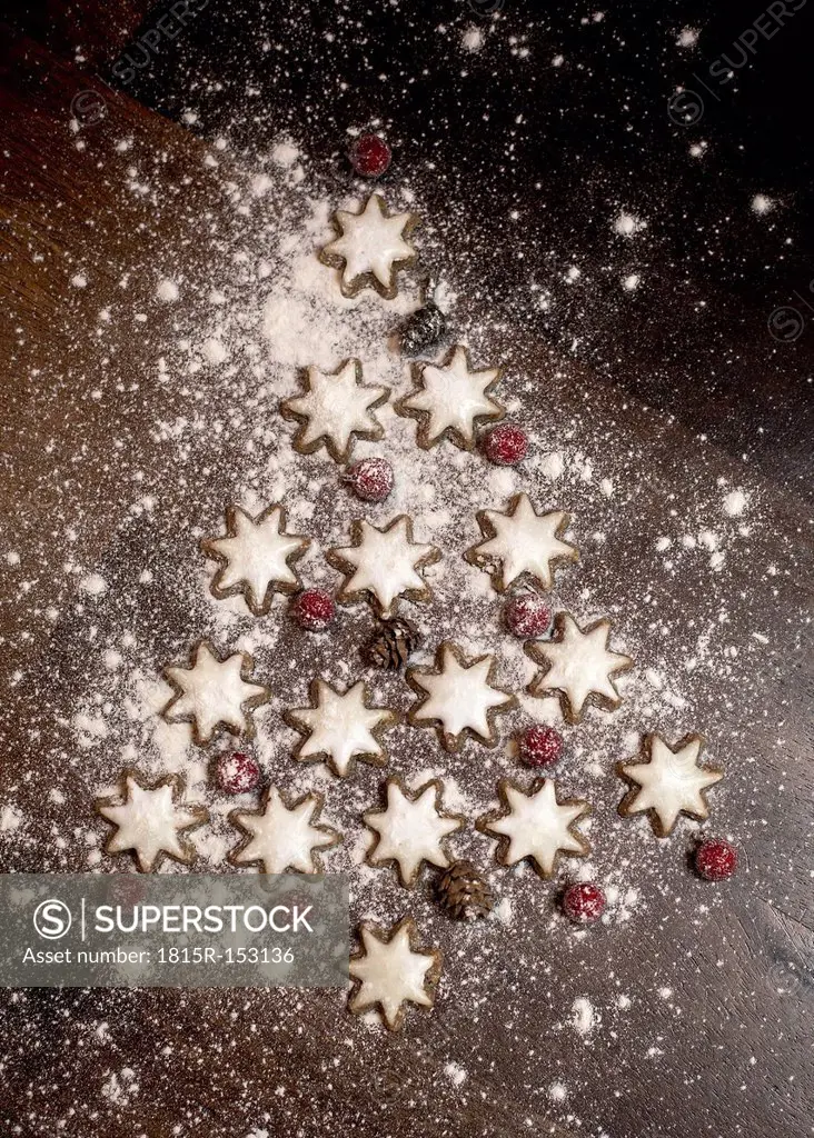 Christmas tree formed of star-shaped cinnamon cookies, red berries and fir cones on wooden table