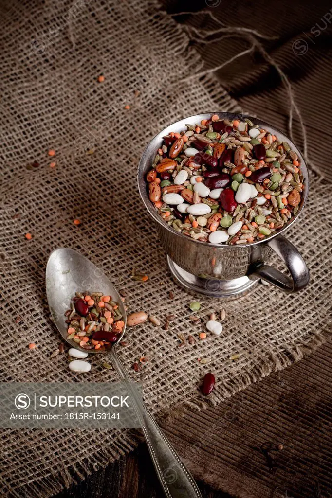 Minestrone mixture (mixed pulses and grain) in small white bowl and a spoon on jute fabric, close-up