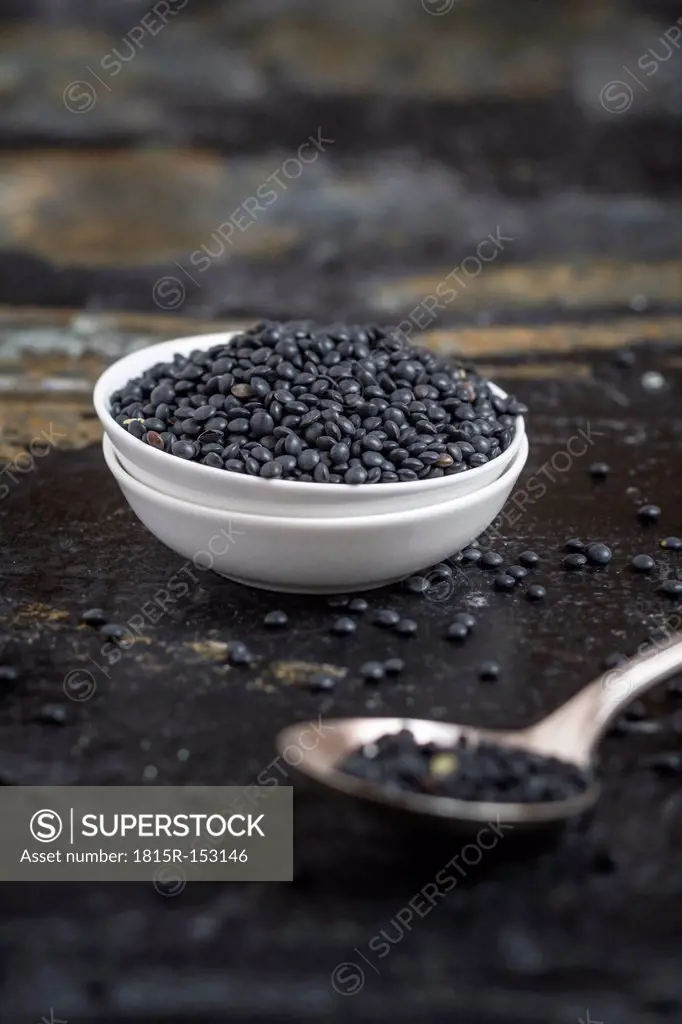 Beluga lentils in small white bowl and a spoon on dark surface, close-up
