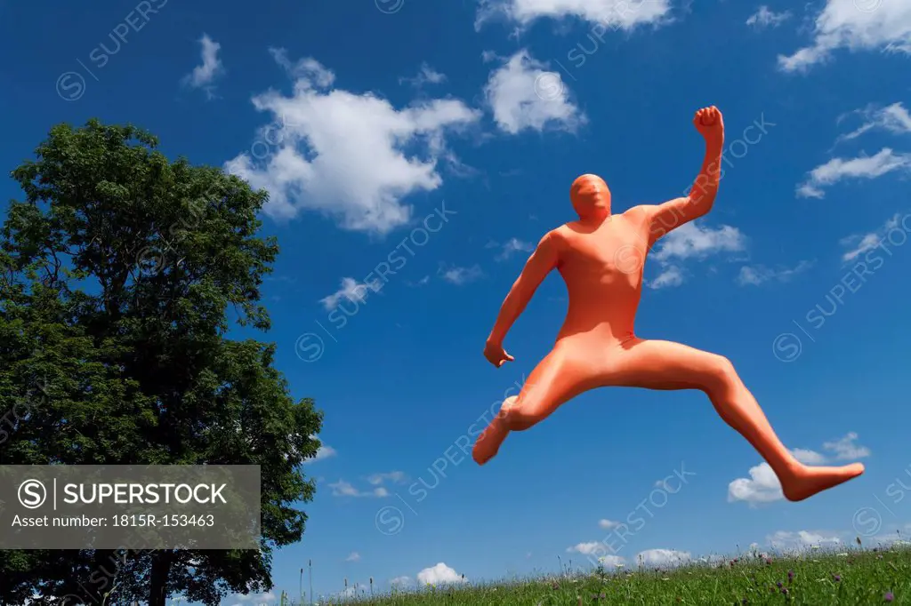 Germany, Bavaria, Man in orange zentai jumping in landscape