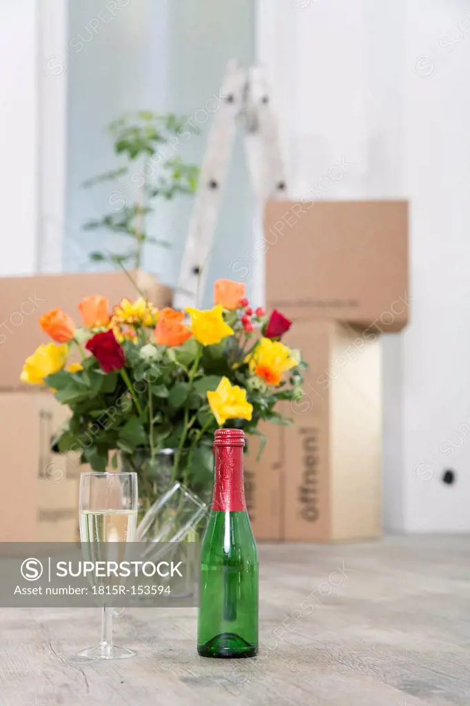 Cardboard boxes, champagne and bunch of flowers in new home