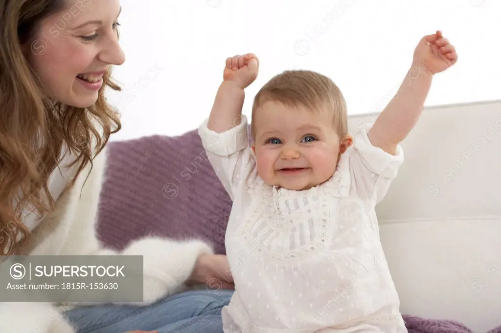 Smiling baby girl with outstrechted arms beside her mother