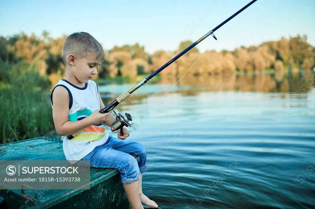 Back view of little boy with fishing rod sitting on boat - SuperStock