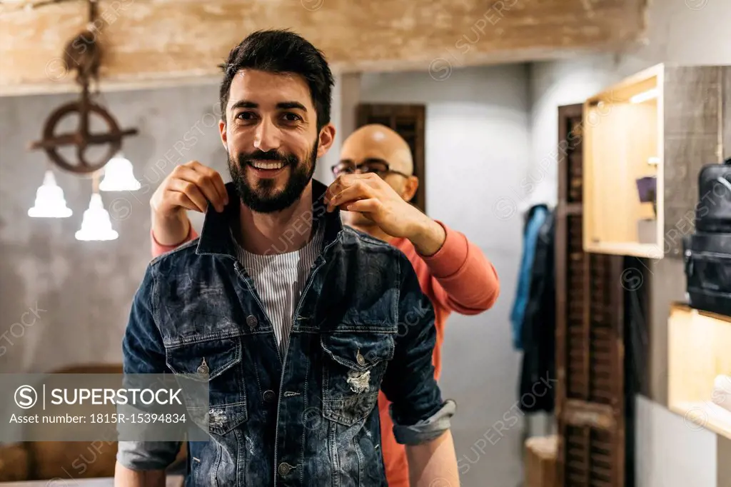 Handsome man trying on new denim jacket with stylist in modern boutique