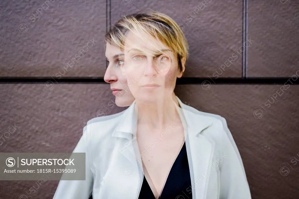 Blond businesswoman leaning against wall, dopple exposure