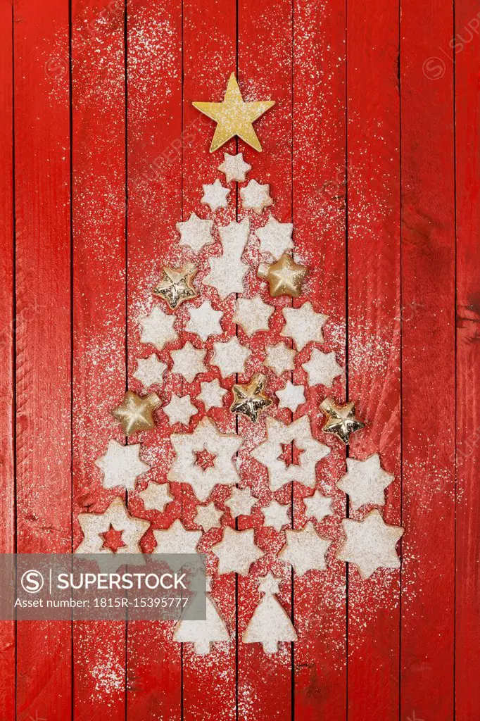 Christmas cookies and star-shaped Christmas baubles forming Christmas tree on red wooden background