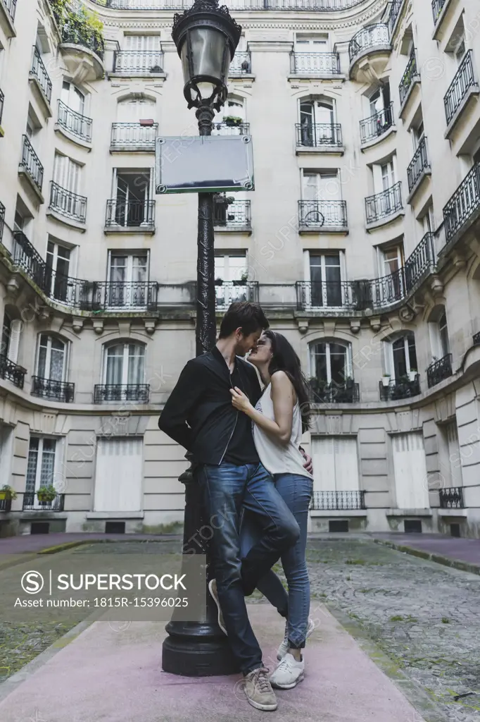 France, Paris, young couple in love standing at street lantern in front of urban building