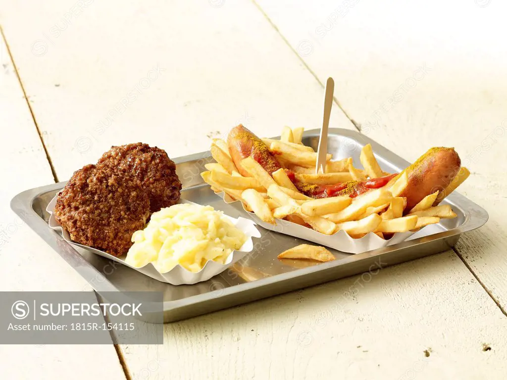 Curry sausage with French fries, two meatballs and mashed potatoes on metal tray