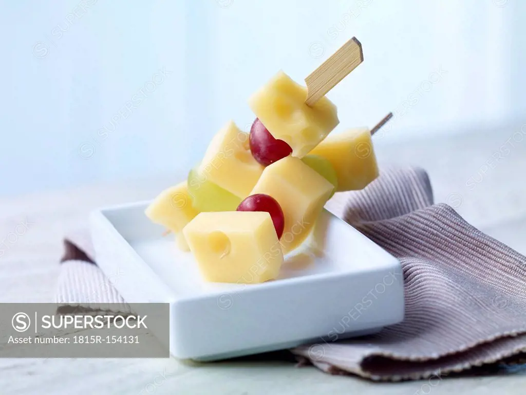Skewered diced Emmentaler cheese with grapes on wooden table
