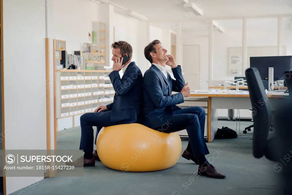 Two businessman checking smartphone with yellow fitness ball in foreground
