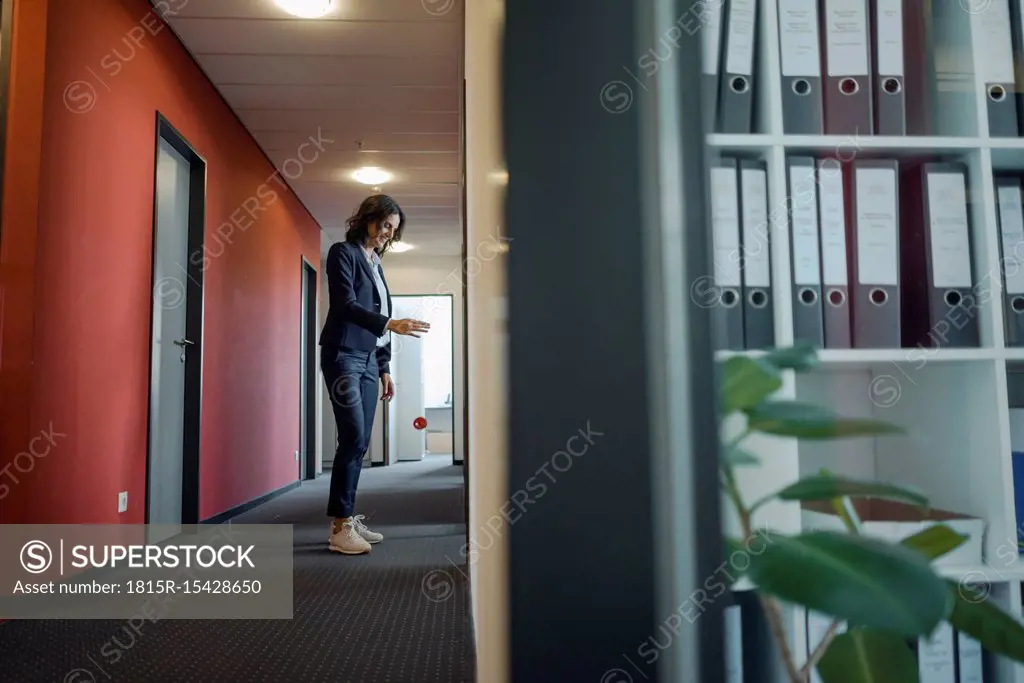 Mature businesswoman standing in office corridor, playing with yoyo