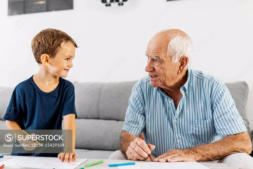 Grandfather and grandson drawing together with coloured pencils at home