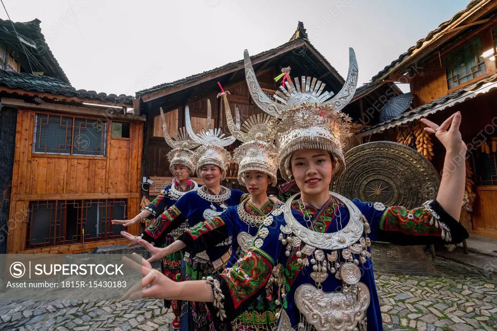 China, Guizhou, Miao women wearing traditional dresses and headdresses posing on village square
