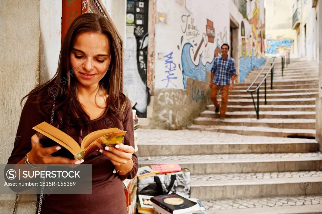 Portugal, Lisboa, Baixa, Rua do Madalena, young woman with book standing in front of antiquarian bookshop
