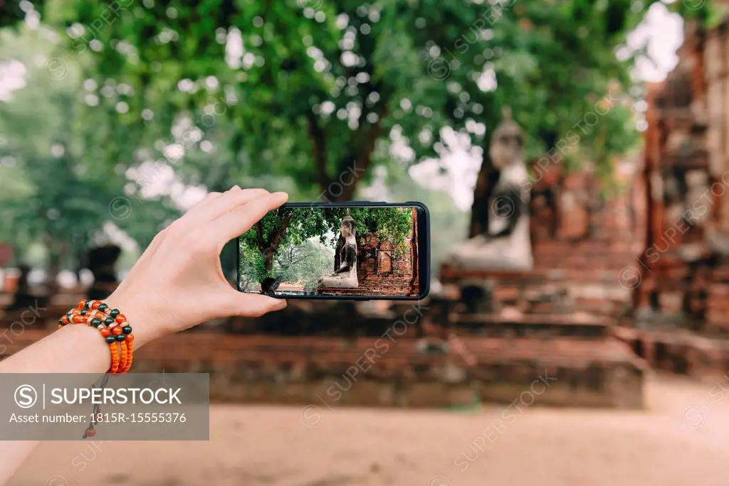 Thailand, Ayutthaya, Woman taking a photo of a Buddha statue at Wat Mahathat