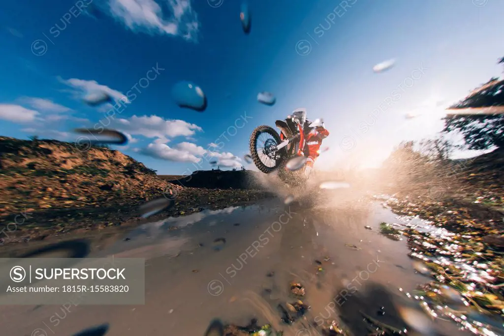 Motocross driver driving through the water, splashing