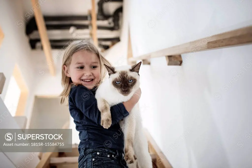 Portrait of little girl with her Siamese cat at home