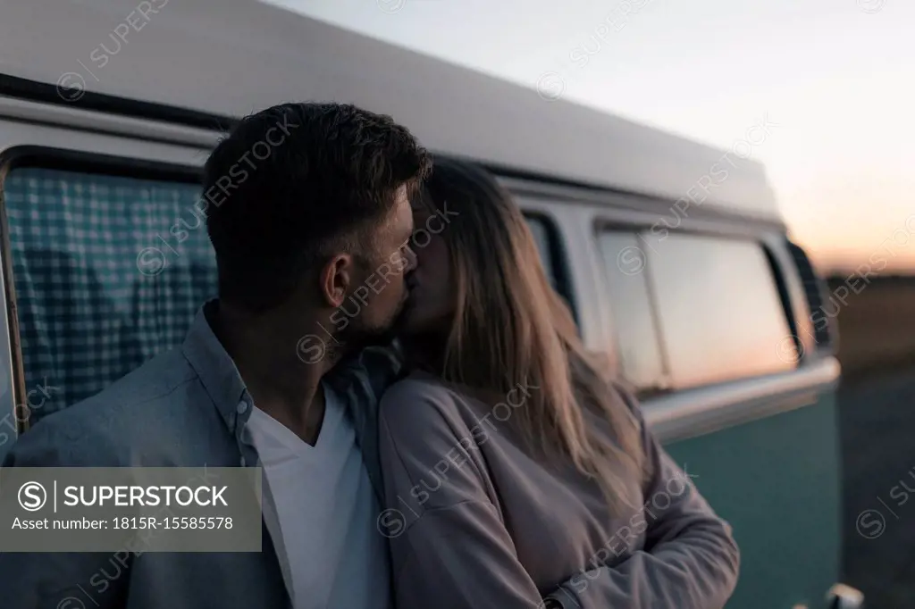Young couple kissing at camper van at dusk