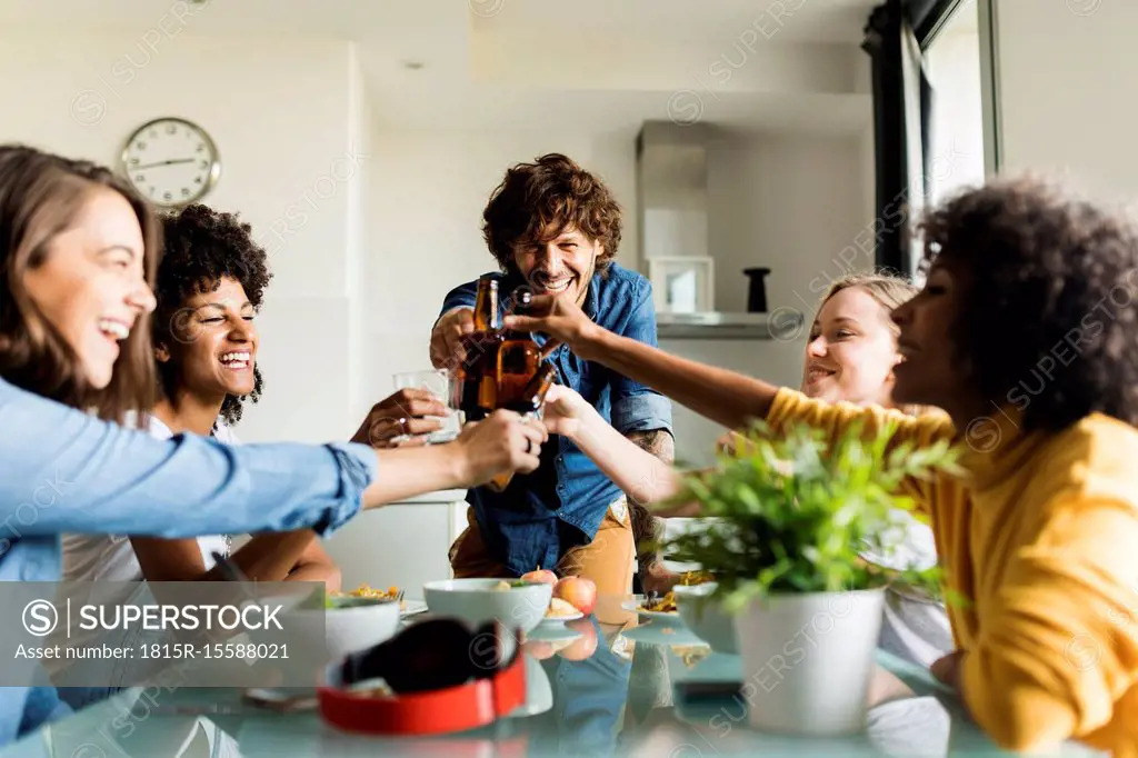 Cheerful friends clinking beer bottles at dining table
