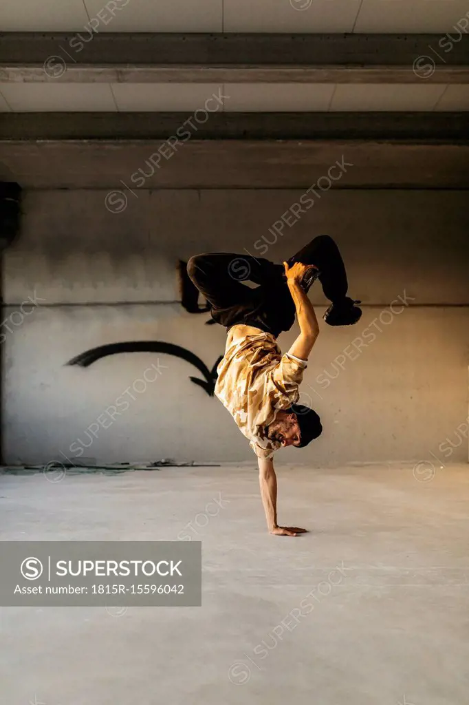 Man doing breakdance in urban concrete building, standing on hand