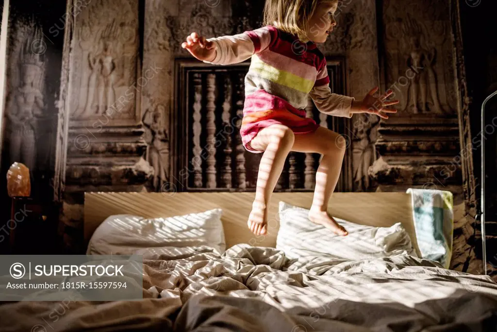 Little girl jumping on parent's bed at home
