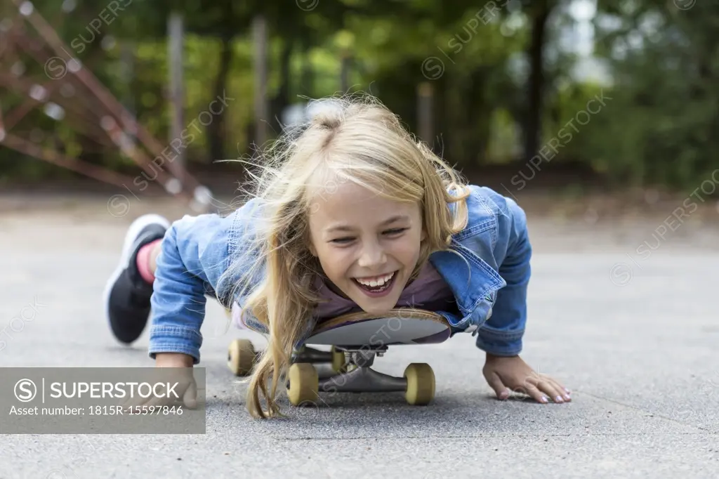 Portrait of laughing blond girl lying on her skateboard outdoors