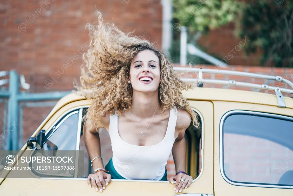 Portrait of blond woman leaning out of window of classic car tossing her hair
