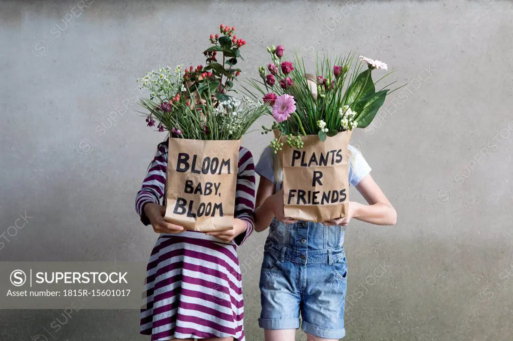 Two girls standing side by side hiding behind paper bags with flowers