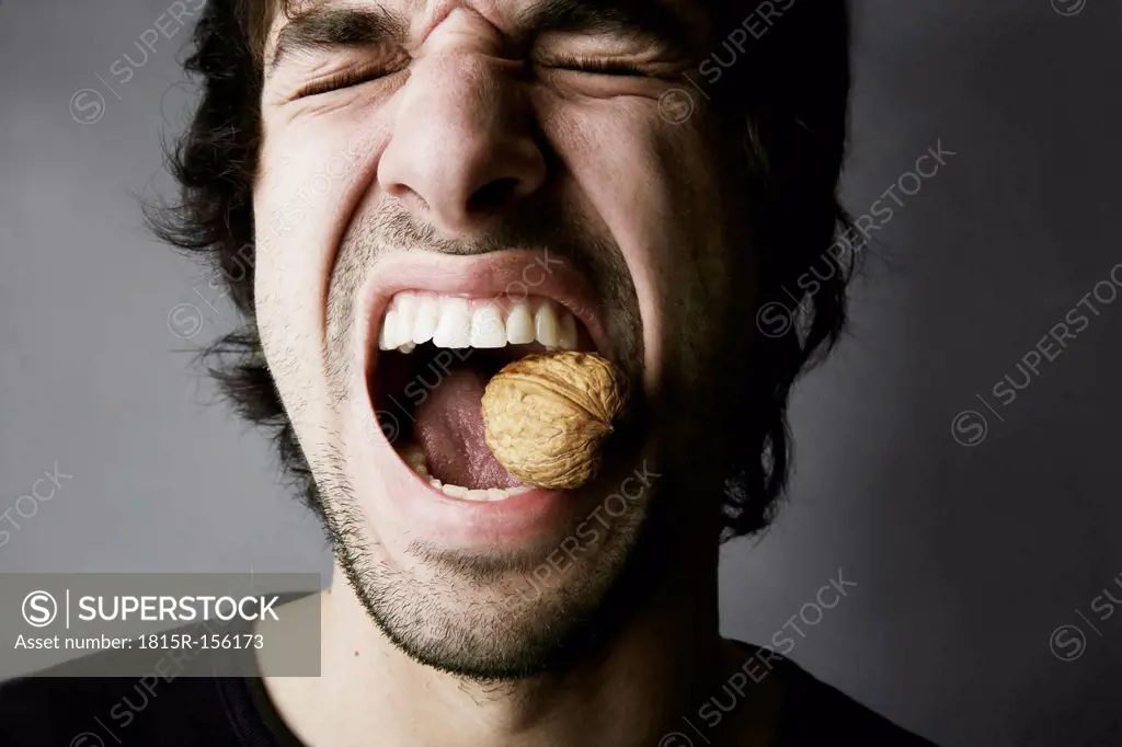 Portrait of young man trying to crack a walnut with his teeth, studio shot