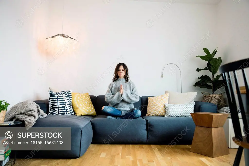 Mature woman sitting cross-legged on couch with eyes closed, meditating at home