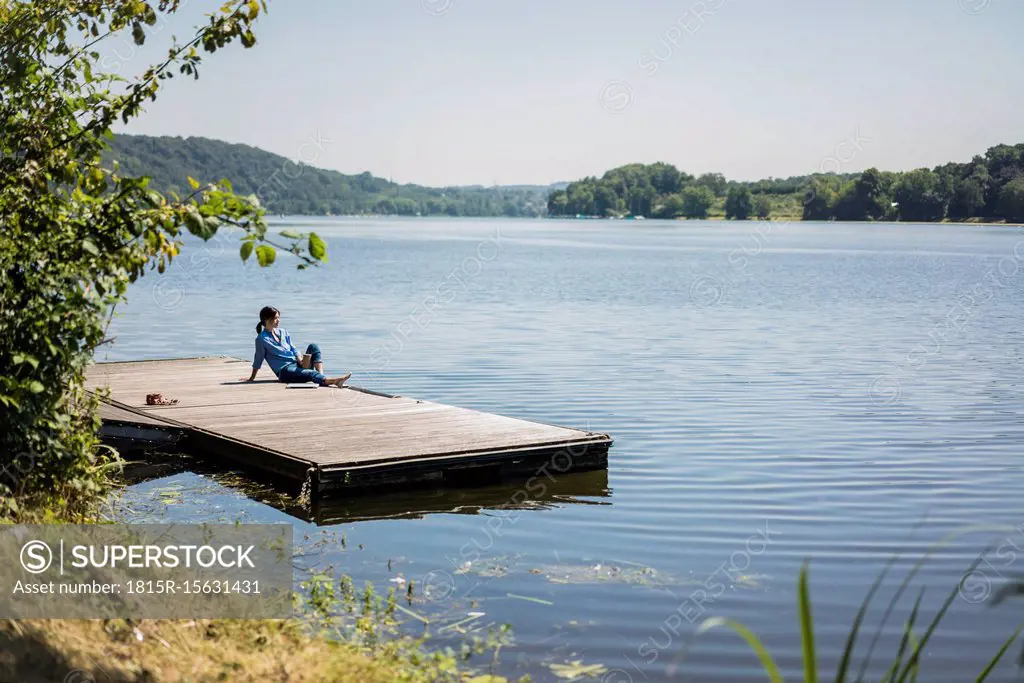 Mature woman sitting on a jetty at a lake, taking a break