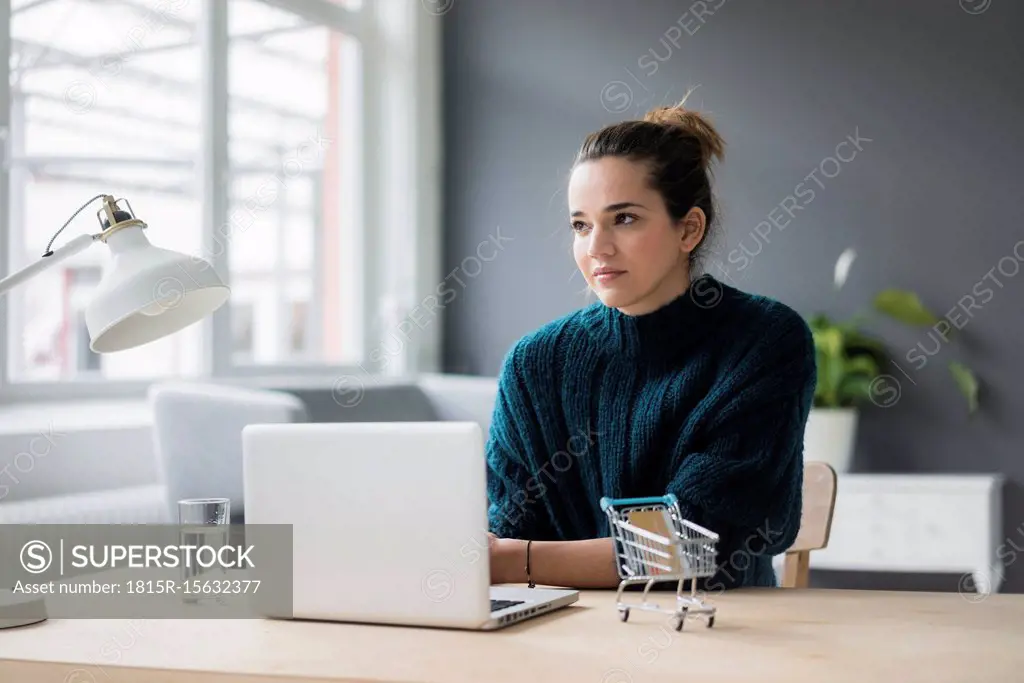 Portrait of pensive woman with laptop and credit card sitting at desk at home