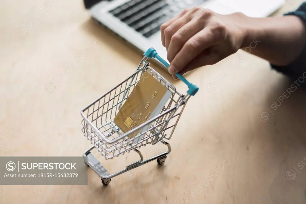 Woman's hand holding mini shopping cart with credit card