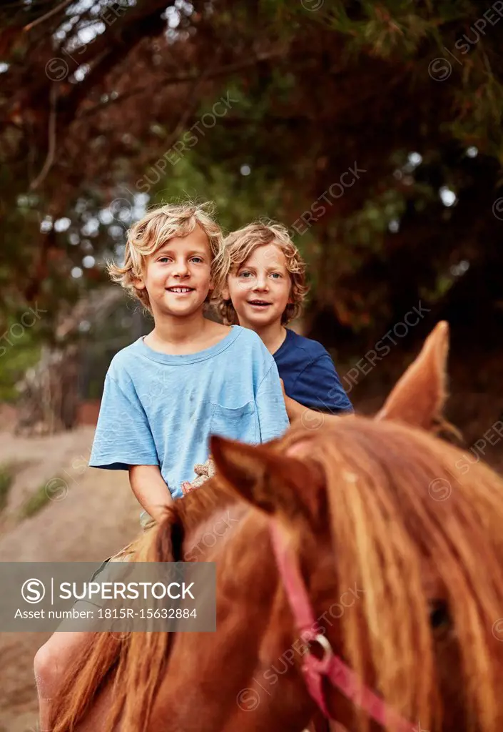 Portrait of two happy boys on horse in a forest