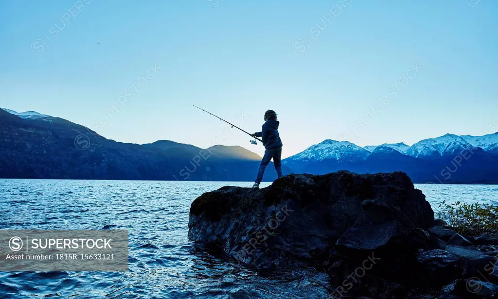 Argentina, Patagonia, Lago Futalaufquen, boy fishing in lake at dusk