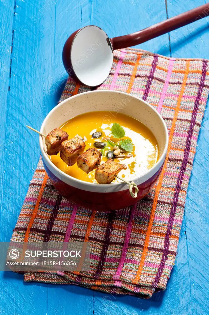 Creamed pumpkin soup in bowl with chicken skewer