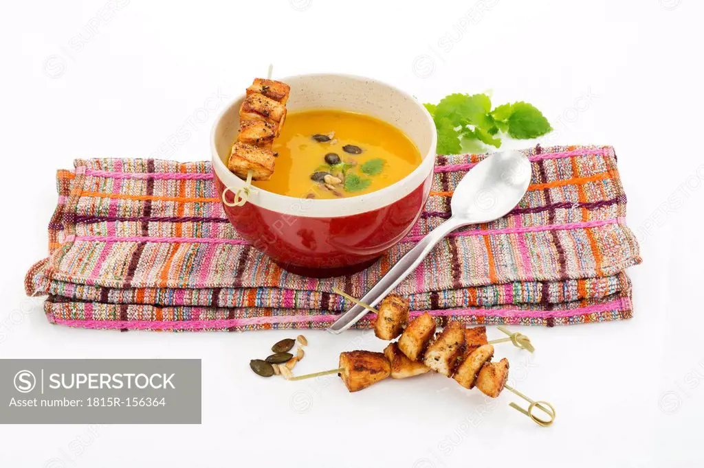 Creamed pumpkin soup in bowl with chicken skewer